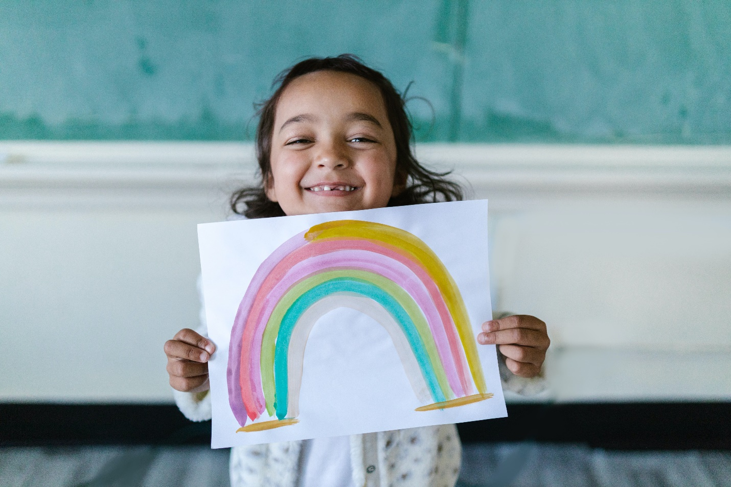 A smiling child holds a painting of a rainbow